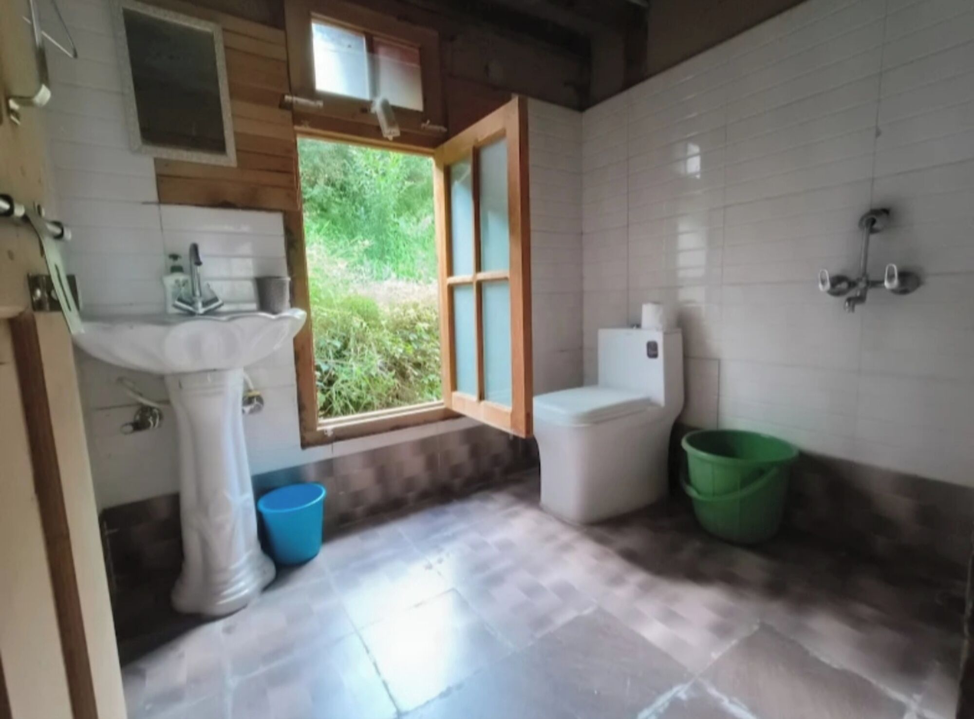Un baño con lavamanos, inodoro y ducha blancos. Se ve un ventanal con vistas a la vegetación.
