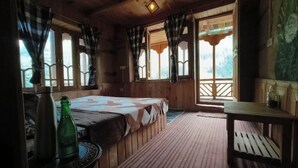 Una habitación cálida tipo cabaña con cama, una mesita y un banco. Hay cortinas en las ventanas, y una botella sobre la mesa.