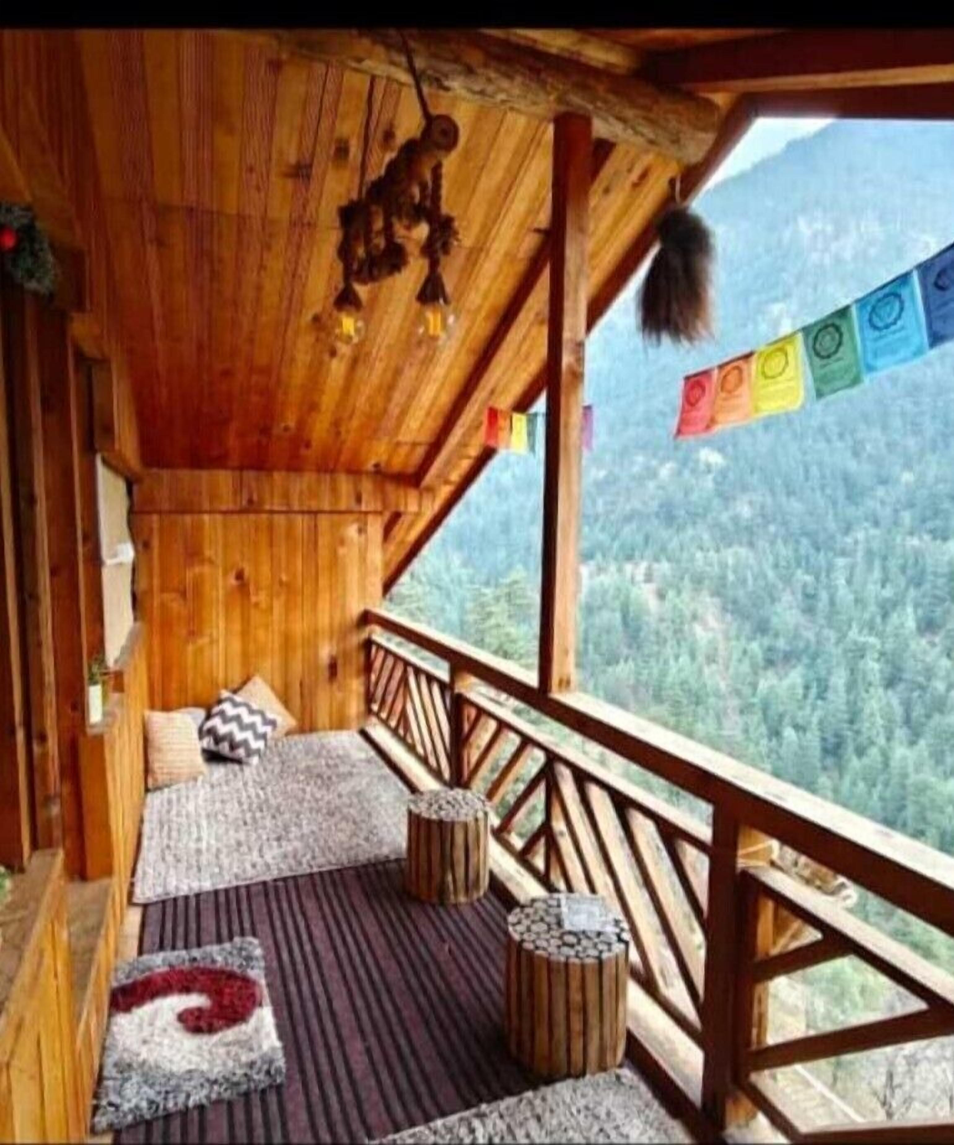 A wooden cabin with a balcony overlooking a forested valley.
