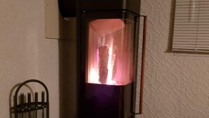 Una chimenea moderna con recinto de vidrio, un soporte metálico y una ventana con persianas.