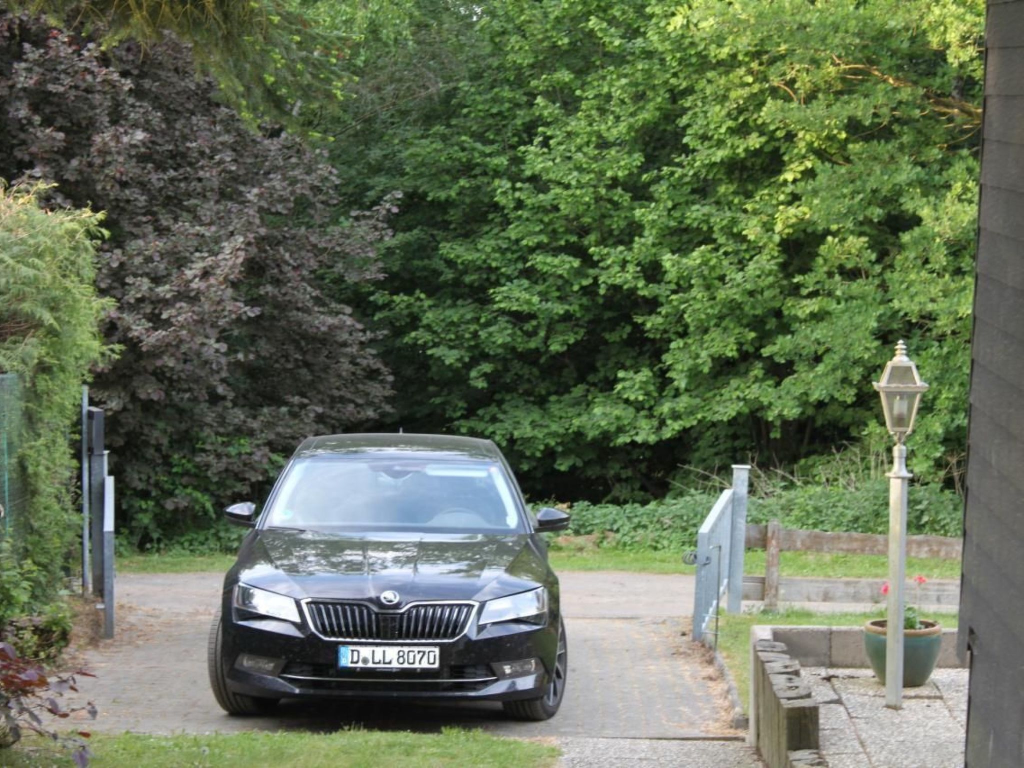 A black car parked in a driveway with a gate and a lamp post in the background.