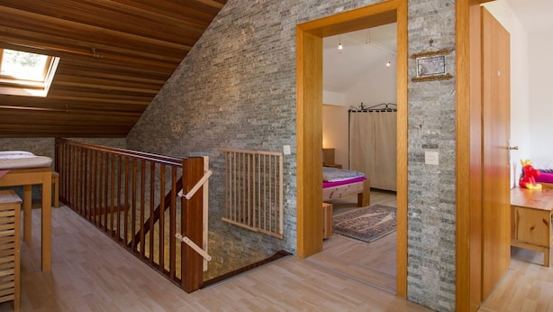 A loft bedroom with a sloped ceiling, wooden beams, a stone wall, a bed with a canopy, and a small desk area. - Gemütliches Ferienhaus in Hasenfeld mit Großem Garten by Interhome (Hasenfeld)
