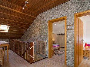 Une chambre située dans un espace de type « loft », avec un plafond en pente, des poutres en bois, un mur en pierre, un lit à baldaquin et un petit coin bureau.