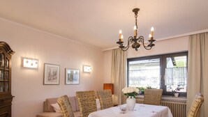 A dining area with wicker chairs, a table with a white tablecloth, a chandelier, and framed pictures on the wall. - Gemütliches Ferienhaus in Hasenfeld mit Großem Garten by Interhome (Hasenfeld)