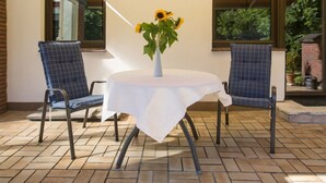 An outdoor patio with a round table, two blue chairs, and a vase with sunflowers. - Gemütliches Ferienhaus in Hasenfeld mit Großem Garten by Interhome (Hasenfeld)
