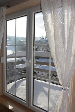 Ein Zimmer mit einer großen Schiebeglasdoor zu einem Balkon mit Blick auf eine verschneite Landschaft.