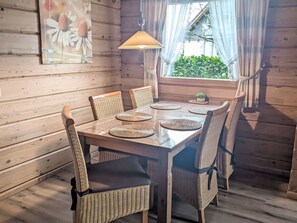 En inredning med trädetaljer, ett matbord, flätade stolar, en hängande lampa och ett fönster med gardiner.