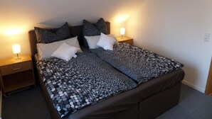 Een net opgemaakt bed met een bedsprei met patroon, twee nachtkastjes met lampen, en een effen muur.