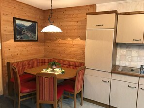Une cuisine de taille réduite avec des murs en bois, une table à manger entourée de chaises à revêtement rouge, un luminaire suspendu et un pare-éclaboussures carrelé au-dessus de l’évier.