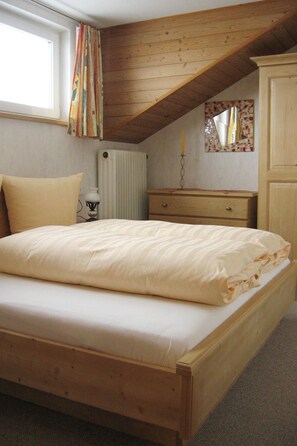 Une chambre avec un lit en bois, une commode, un radiateur et une fenêtre avec des rideaux.