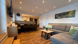 A modern living room with a grey sofa, wooden coffee table, and a dining area with a wooden table and chairs. - Barbara by Interhome (Bichlbach)