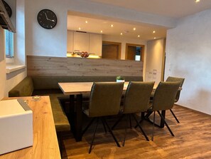 A modern dining area with a wooden table and four chairs, a clock on the wall, and a kitchen in the background. - Barbara by Interhome (Bichlbach)