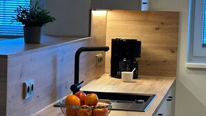 A modern kitchen with a wooden countertop, a black coffee maker, a bowl of fruit, and a potted plant. - Barbara by Interhome (Bichlbach)