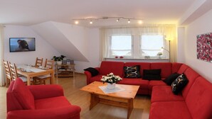 Een woonkamer met een rode bank, een houten salontafel, en een eethoek met een tafel en stoelen.
