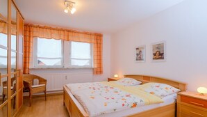 Een slaapkamer met een houten bed, twee nachtkastjes, een stoel en een raam met gordijnen.