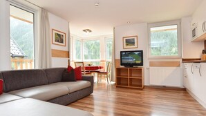 Un salon moderne avec un canapé, un téléviseur, un plancher en bois et de grandes fenêtres.