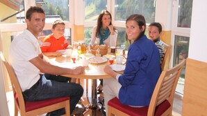 Un coin repas avec une table et des chaises en bois, de grandes fenêtres donnant sur un paysage verdoyant et un luminaire au plafond.