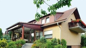 Et toetagers hus med en overdækket veranda, murstensfacade og en lille have med trapper til indgangen.