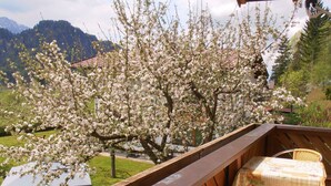 Ein Balkon mit Holzgeländer, einem Tisch mit blumigem Tischtuch und Stühlen.