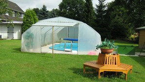 Una estructura tipo invernadero con una piscina en su interior, rodeada de un césped y un banco de madera.