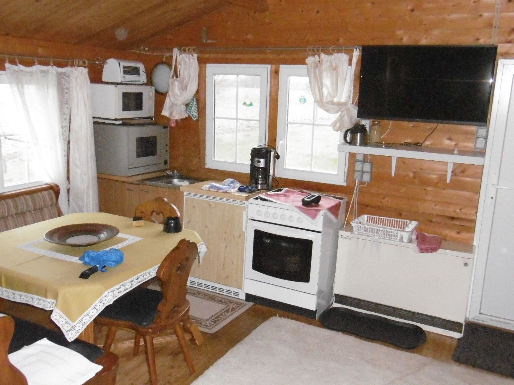 A cozy cabin-style kitchen with a dining area, wooden walls, a microwave, a stove, and a television.