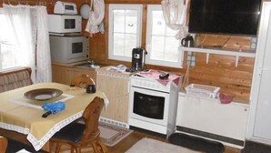 Una cocina acogedora de estilo cabaña con comedor, paredes de madera, un microondas, una estufa y un televisor.
