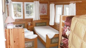 Un dormitorio de cabaña de madera con una cama individual, una mesita de noche con lámpara y una ventana con cortinas.