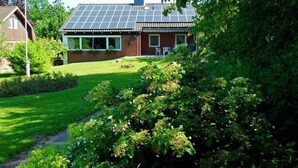 Una casa con paneles solares en el techo, una bandera y un jardín bien cuidado.