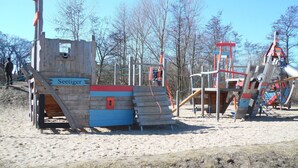 Un parque infantil con tobogán y estructuras para escalar, rodeado de árboles.