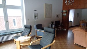 Una habitación con dos sillas de madera, una mesa de madera, un sofá, un televisor y un radiador.