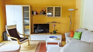 A living room with a sofa, armchair, TV, and a bookshelf. - Apartment Bergblick by Interhome (Abtenau)