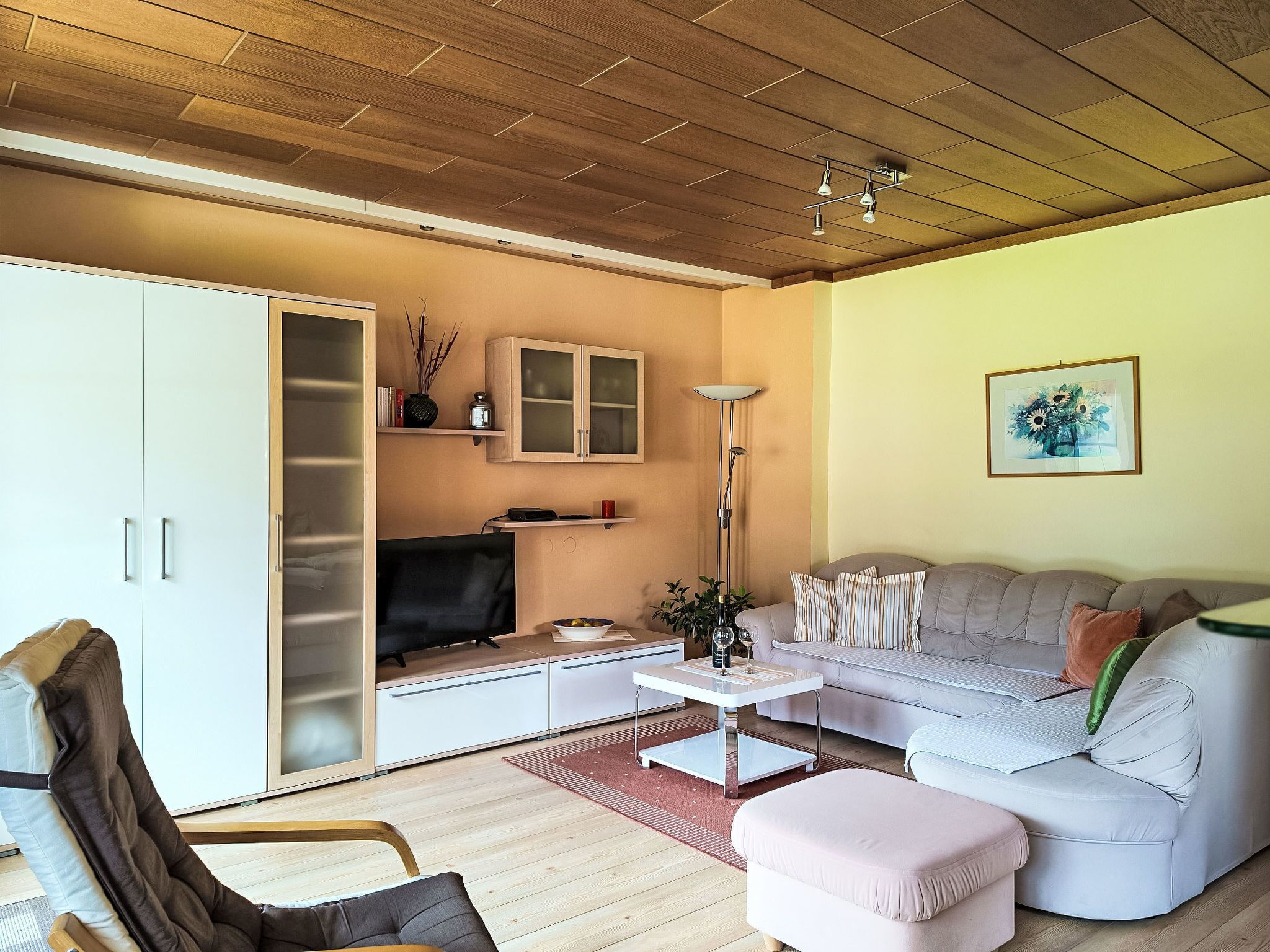 Ein Wohnzimmer mit Sofa, Couchtisch, Fernseher, Schrank und Stehlampe.