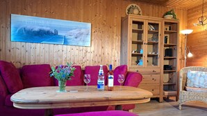 Een gezellige kamer met een houten wand, een ronde houten tafel met een bloevas, twee wijnglazen en een waterfles.