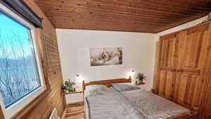 Een slaapkamer met houten lambrisering, een bed, een raam, een aan de muur hangend schilderij en een garderobe.