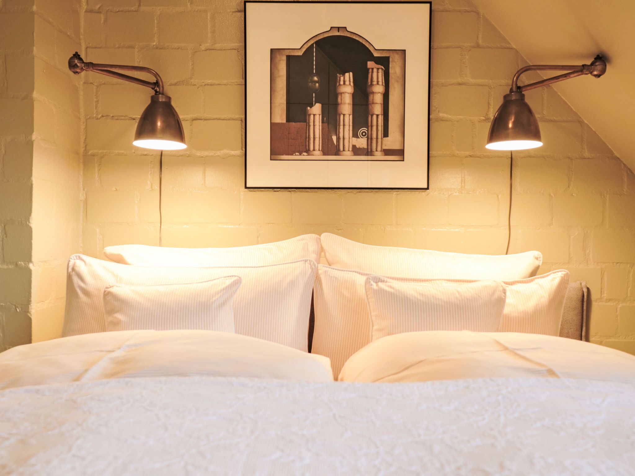 Een slaapkamer met een bakstenen muur, een lijst met een foto boven het bed, en twee wandlampen.