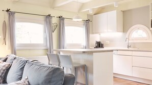 Une cuisine moderne dotée d’un îlot central, de meubles blancs et d’un coin repas avec un canapé et des chaises gris.