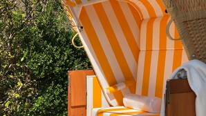 Une chaise longue avec un tissu rayé orange et blanc, une chaise en osier et une porte en bois.