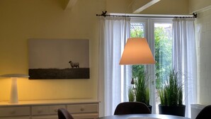 Un coin repas comprenant une table, des chaises, une lampe, un tableau et une fenêtre avec des rideaux.