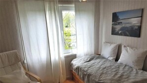 A bedroom with a bed, a chair, a window, and a painting on the wall. - Villa Bullerbü by Interhome (Norrhult)