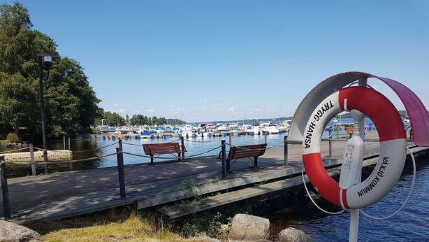A wooden pier with benches, a lifebuoy, and a marina with boats in the background. - Villa Bullerbü by Interhome (Norrhult)