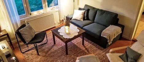 A cozy living room with a sofa, two armchairs, a coffee table, and a window with a view of greenery.