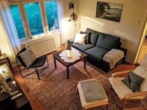 A cozy living room with a sofa, two armchairs, a coffee table, and a window with a view of greenery.