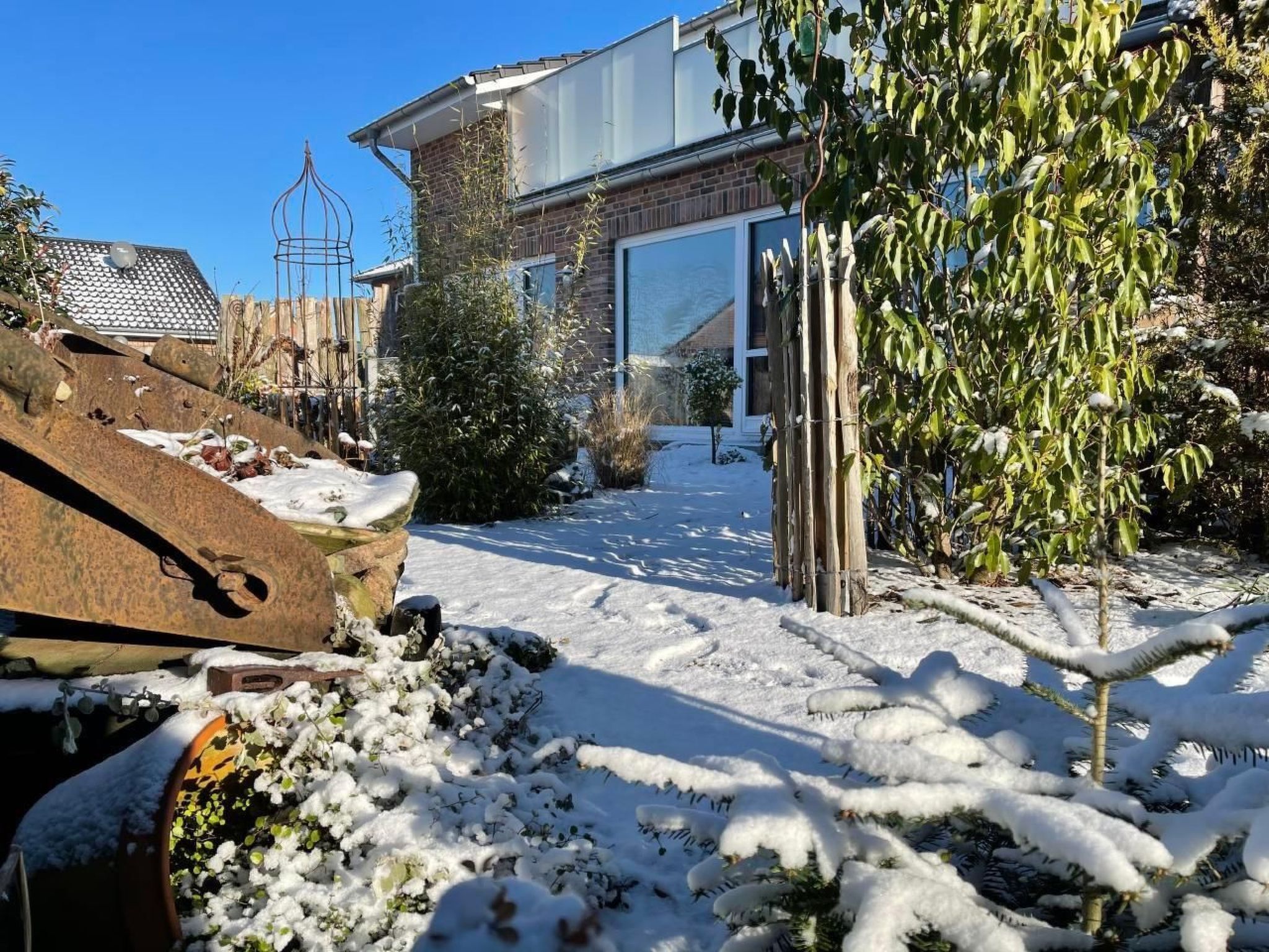 En bostadsfastighet med en snötäckt trädgård, ett hus byggt av tegel och ett staket av metall.