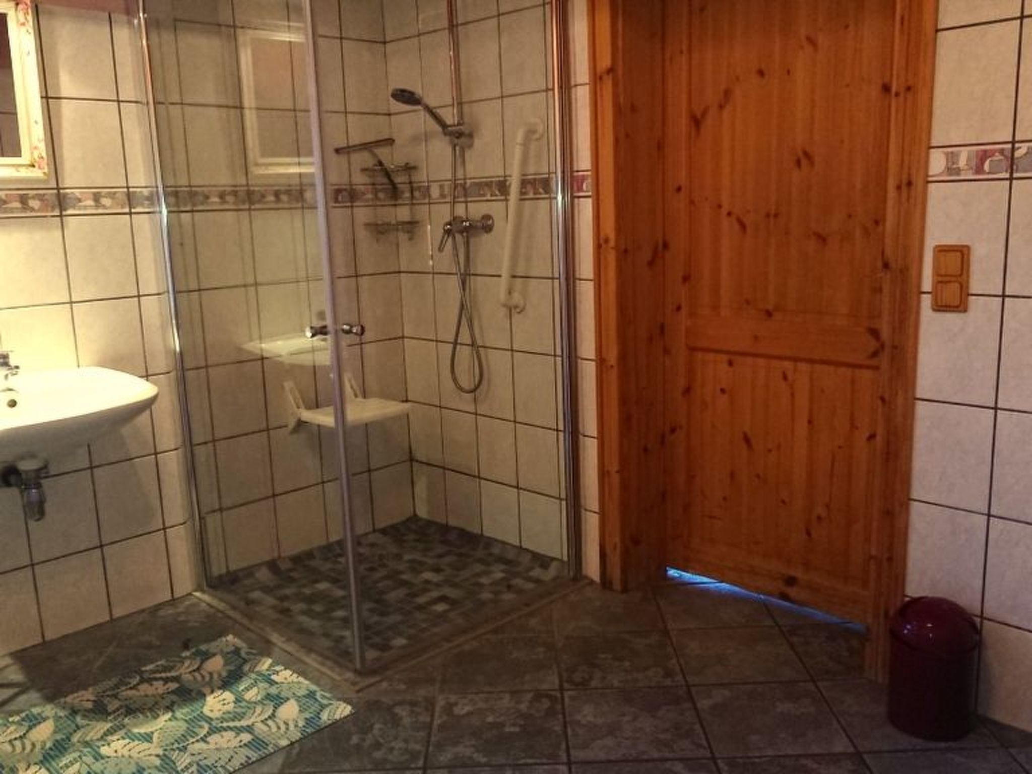 Kylpyhuoneessa on lasiseinällä varustettu suihku, pesuallas ja puuovi.
