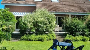 Ein Haus mit einem Ziegeldach, einem Backsteinsschornstein und einer überdachten Veranda mit Tisch und Stühlen.