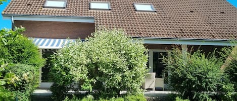A house with a tiled roof, a brick chimney, and a covered porch with a table and chairs.