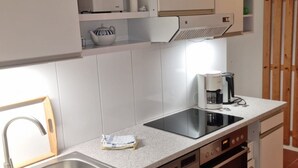 Eine kompakte Küche mit weißen Schränken, einer Edelstahl-Spüle, einem Geschirrspüler und einer Kaffeemaschine.