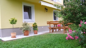 A yellow building with a patio area, a wooden bench, and potted plants. - Ruhige Ferienwohnung in Feld am See by Interhome (Feld am See)