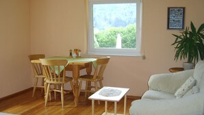 A dining area with a table and chairs, a small cart, a window with a view of greenery, and a white sofa. - Ruhige Ferienwohnung in Feld am See by Interhome (Feld am See)