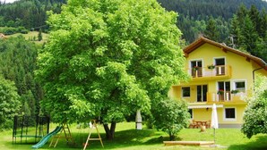 A yellow two-story house with a balcony, surrounded by lush greenery and a mountain in the background. - Ruhige Ferienwohnung in Feld am See by Interhome (Feld am See)